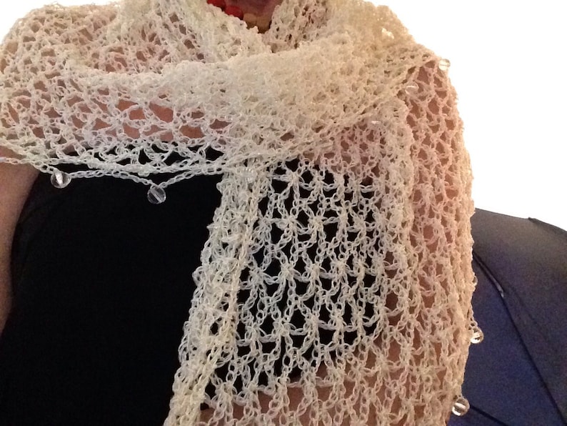 May include: A white crocheted shawl featuring an open, airy lattice stitch pattern. The edges of the shawl are finished with small, clear, spherical beads attached at regular intervals along the border, creating a delicate, textured appearance.