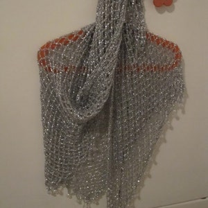 Silver shawl on an orange hanger, front view of the openwork crochet and shimmering weave.