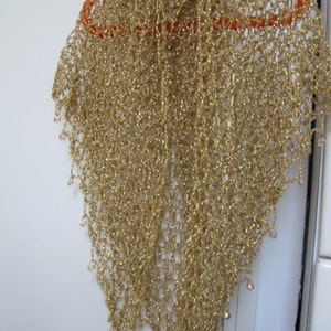 Champagne gold lurex shawl on an orange hanger against a white door, full-length view of the shimmering drape.
