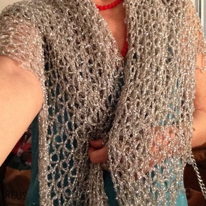 Front view of the silver crocheted lurex shawl draped over a turquoise dress, one hand resting at the waist, showing the open stitchwork.