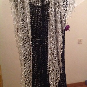 Silver lurex crochet shawl layered over a black fringed dress on a hanger, full-length view of the sparkling wrap.