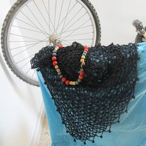 Black beaded shawl on a blue dress, photographed with a bicycle wheel in the background.
