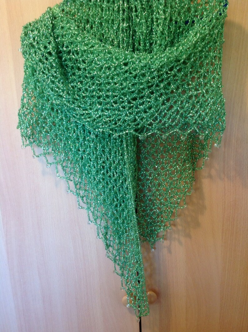 Bright green lurex shawl hanging on a wooden door, draped to a long point.