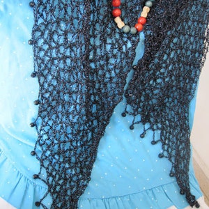 Black shawl draped over a light blue ruffled dress, styled with a colorful beaded necklace.