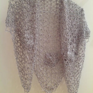 Silver floral shawl hanging flat on a hanger, full view of the openwork and scattered flower motifs.