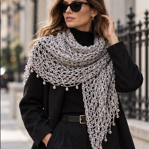 Woman in a black outfit wearing the silver beaded shawl, iron fence and city street in the background.