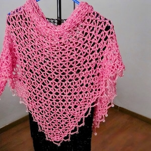 Pink lurex crochet shawl on a hanger over a black dress, full view of the shimmering openwork wrap.