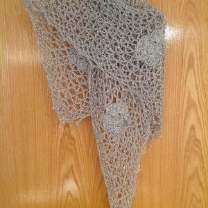 Silver floral shawl on a wooden door, draped to a point with a crocheted flower applique near the hem.