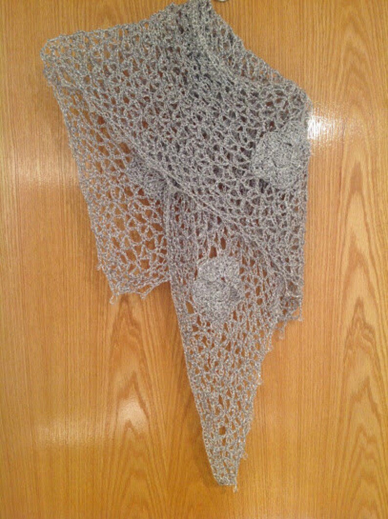 Silver floral shawl on a wooden door, draped to a point with a crocheted flower applique near the hem.