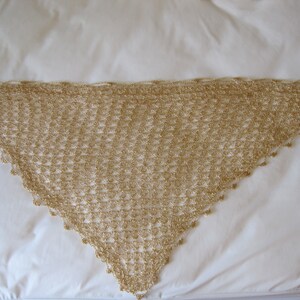 Flat lay of the gold lurex crochet shawl from a second angle, showing the pointed hem and delicate beadwork along the border.