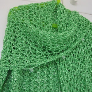 Bright green lurex crochet shawl hanging in a soft cowl fold, close view of the openwork stitches.