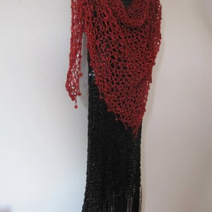 Red shawl draped over a black fringed dress on a hanger, full-length view of the sparkling wrap.