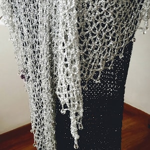 Silver beaded shawl draped over a black dress on a hanger, side view of its long flowing drape.