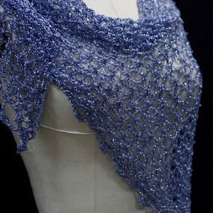 May include: A periwinkle blue shawl featuring an open, loose crochet stitch pattern with a subtle metallic shimmer throughout the yarn. The triangular garment is draped over a mannequin, showcasing the intricate, airy texture of the knit design.