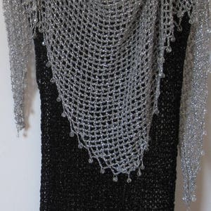 Silver shawl layered over a black dress on a hanger, front view of the sparkling openwork wrap.