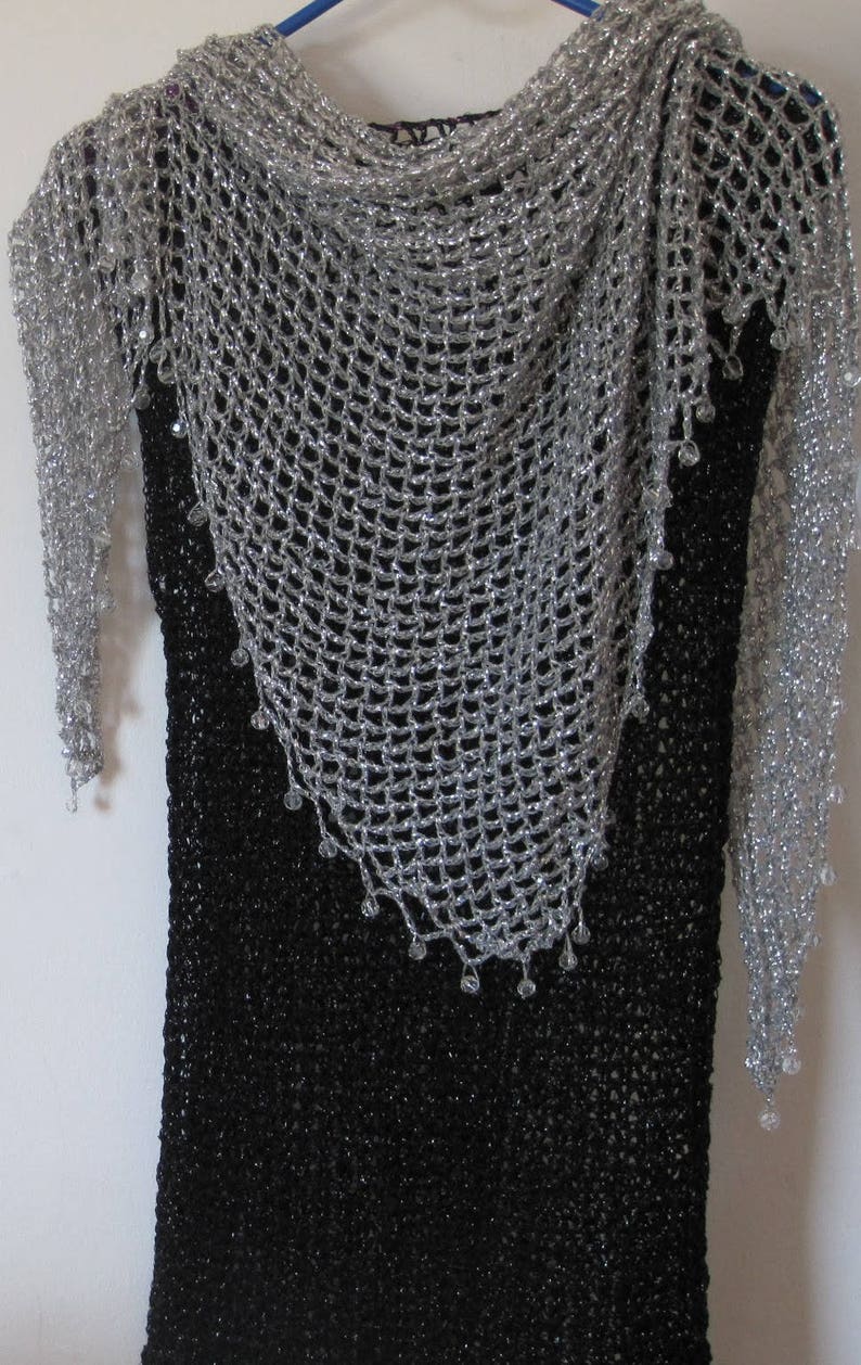 Silver shawl layered over a black dress on a hanger, front view of the sparkling openwork wrap.