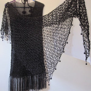 Black lurex crochet shawl draped over a black fringed dress on a hanger, side view of the shimmering wrap.