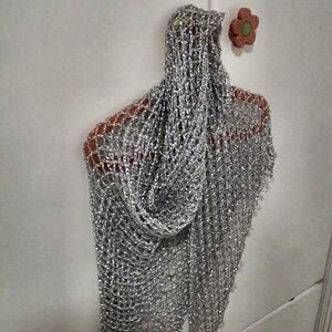 Silver beaded lurex shawl hanging on a red hanger against a white door, folded into a soft cowl drape.
