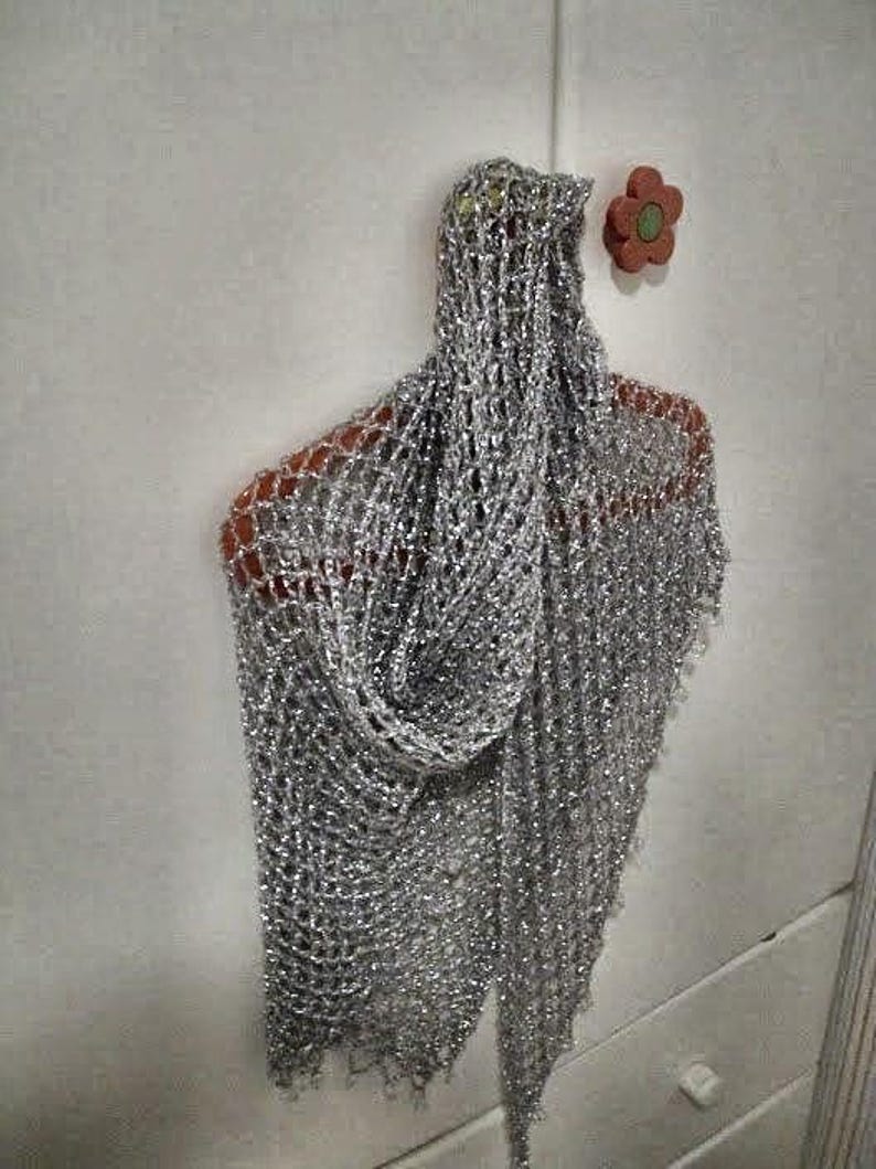 Silver beaded lurex shawl hanging on a red hanger against a white door, folded into a soft cowl drape.