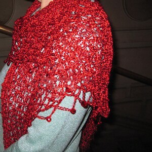 Red lurex shawl worn over the shoulders with a light blue top, close view of the textured crochet stitches.