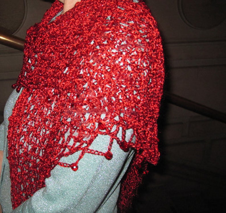 Red lurex shawl worn over the shoulders with a light blue top, close view of the textured crochet stitches.