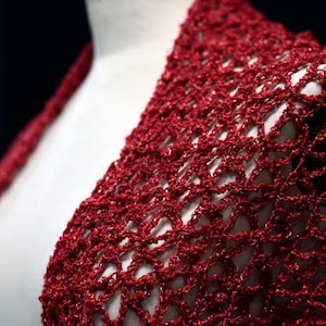 Close-up of the red lurex crochet shawl on a mannequin's shoulder, showing the openwork stitch pattern.