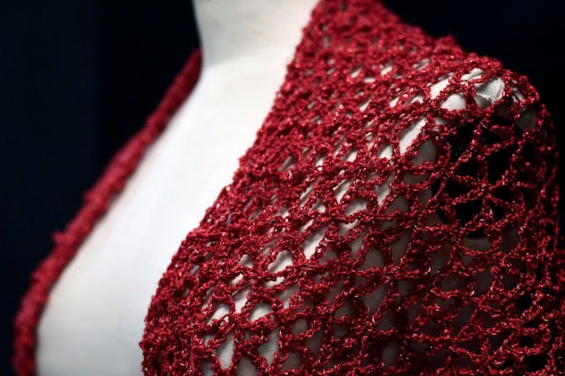 Close-up of the red lurex crochet shawl on a mannequin's shoulder, showing the openwork stitch pattern.