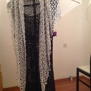 Silver shawl layered over a black fringed dress on a hanger, front view of the sparkling openwork wrap.