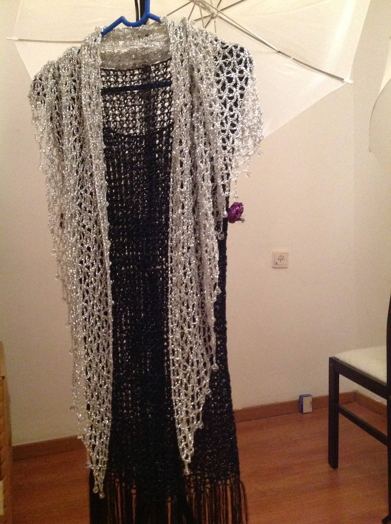 Silver shawl layered over a black fringed dress on a hanger, front view of the sparkling openwork wrap.