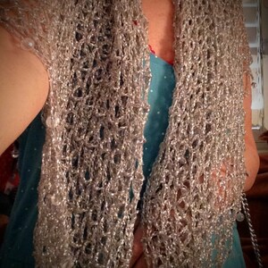 Silver crochet shawl draped over a turquoise dress, front view of the airy open stitches.