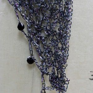 Extreme close-up of the grey lurex crochet texture, with dark beads dangling from the fine stitches.