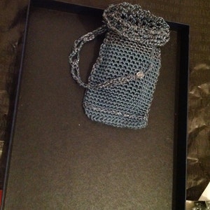 Grey crochet clutch bag resting in a dark gift box, top view of the shimmering evening handbag.