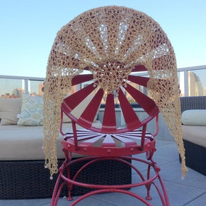 Back view of the gold lurex shawl spread over a red rooftop chair, the city skyline visible beyond the terrace railing.