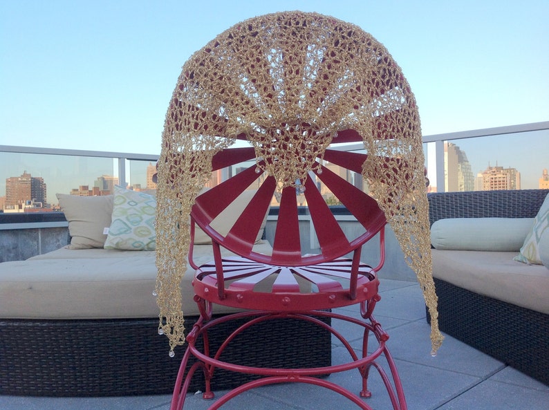 Back view of the gold lurex shawl spread over a red rooftop chair, the city skyline visible beyond the terrace railing.