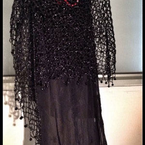 Black shawl layered over a dark dress with a red necklace, front view of the openwork.
