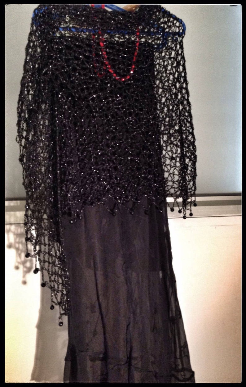 Black shawl layered over a dark dress with a red necklace, front view of the openwork.