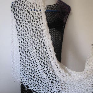 Cream crochet shawl draped over a black dress on a hanger, side view of the airy openwork wrap.