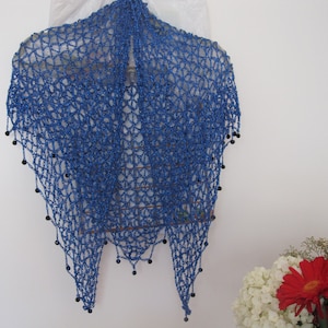 Sapphire blue lurex shawl hanging in a full drape, dark beads along the edge, flowers arranged below.