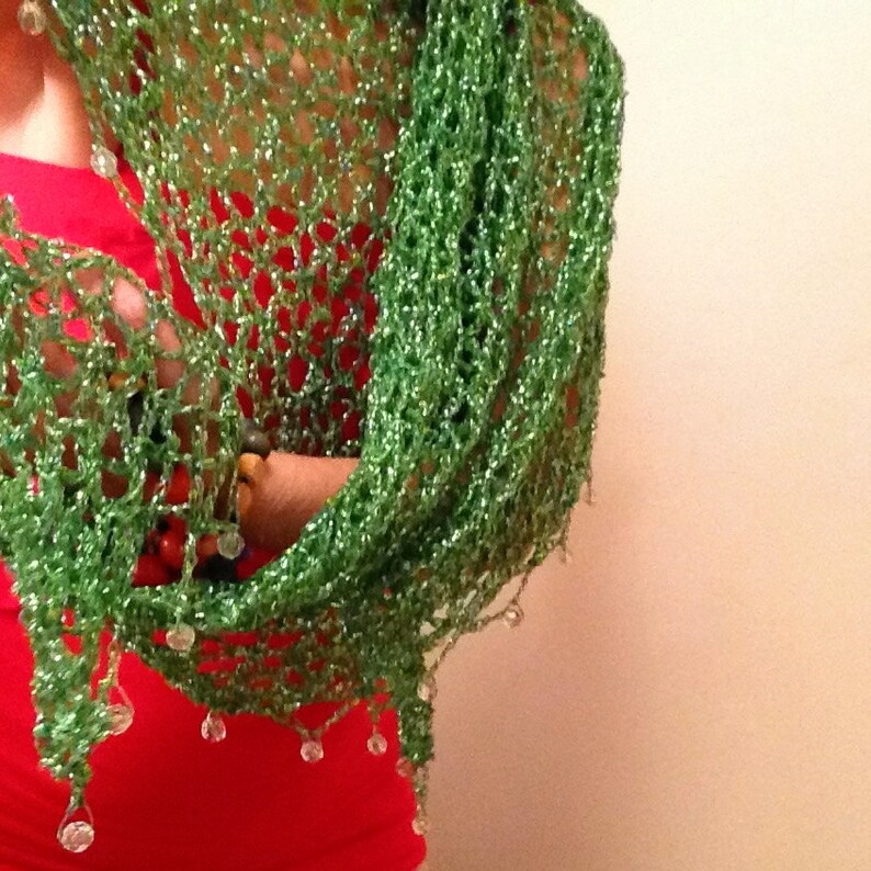Green sparkle lurex shawl worn over a red dress, close view of the openwork crochet and dangling bead trim.