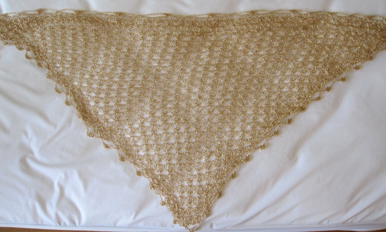 Gold beaded shawl laid flat in a triangle on a white surface, full view of the even crochet stitches and beaded edge.