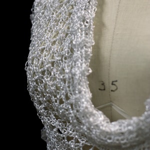 Close view of the white shawl's neckline drape on the mannequin, layered folds of openwork.
