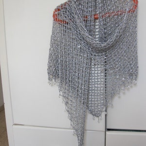 Silver beaded shawl on a red hanger against white closet doors, draped to a long point.