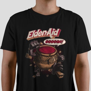 May include: Black t-shirt with a graphic of a cartoon pot with red liquid and the text "EldenAid" in a red and yellow font. The pot has arms and legs and is breaking through a wall of brown bricks. The text "Oooooh!" is in a speech bubble above the pot.