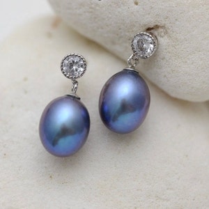 Puede incluir: Un par de pendientes de plata con un pequeño cristal de imitación transparente y una gran perla azul.