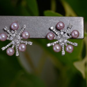 May include: A pair of silver earrings with a starburst design and pink pearls.