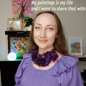 Puede incluir: Una mujer con una blusa morada y un collar floral morado oscuro. La imagen incluye el texto "My paintings is my life and I want to share that with you". Obras de arte y objetos decorativos son visibles en el fondo.