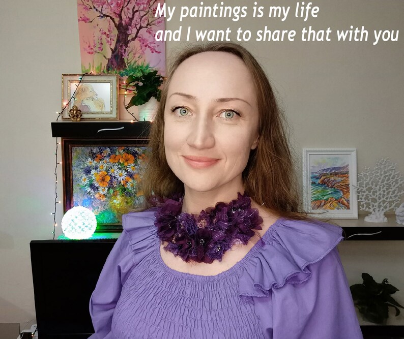 Puede incluir: Una mujer con una blusa morada y un collar floral morado oscuro. La imagen incluye el texto "My paintings is my life and I want to share that with you". Obras de arte y objetos decorativos son visibles en el fondo.