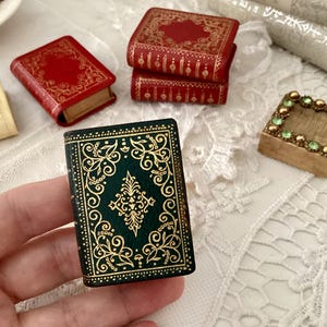 May include: A set of miniature books with gold and red patterned covers. The books are arranged in a stack with the top book being green with a gold pattern.