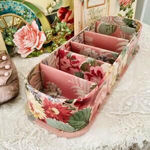 May include: A floral patterned fabric box with five compartments. The box is pink and white with a floral design.