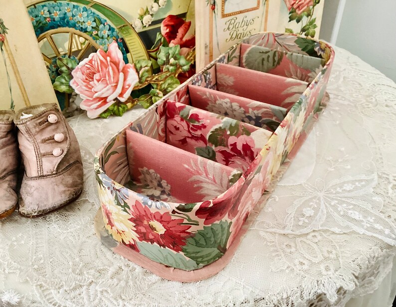 May include: A floral patterned fabric box with five compartments. The box is pink and white with a floral design.